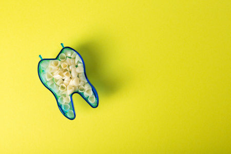 Dental crowns in the shape of a tooth on a yellow background. The concept of manufacturing ceramic hypoallergenic crowns for dental prosthetics in orthodontics. Copy space for text, zirconium dioxideの写真素材