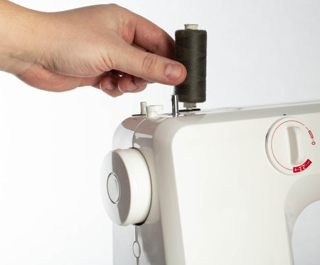 Hand of a seamstress putting a spool of thread on a sewing machine while sewing, industry. Tailoring...