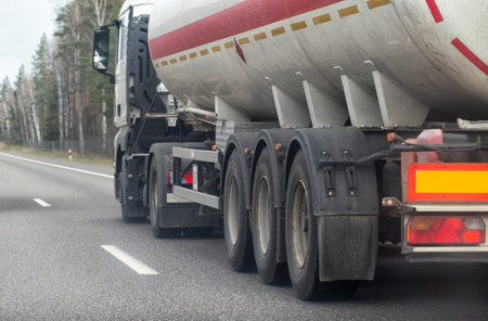 A truck with a semi-trailer tanker transports a dangerous chemical cargo of acid and alkali along a country road in the spring.の写真素材
