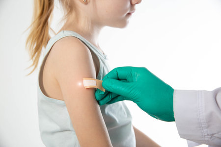 Doctor's hands in green medical gloves stick a plaster on the shoulder of a girl child after vaccination against hemophilus influenzae and pneumococcal. Copy space for text, tuberculosisの写真素材