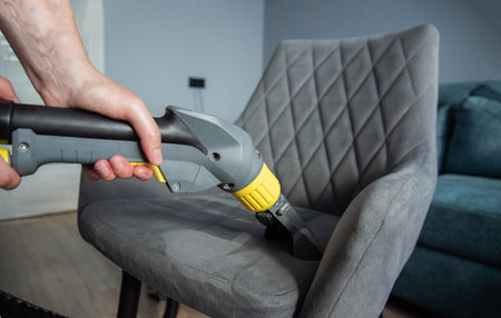 The hands of a girl with a washing vacuum cleaner clean and wash the gray upholstery of a soft chair from dirt. Cleaning services, business. Copy space for textの写真素材