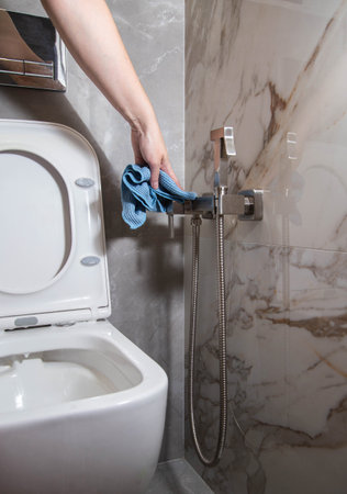 Washing and cleaning the toilet and hygienic shower against the background of porcelain tiles on the wall. Cleaning servicesの写真素材