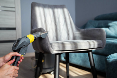 A girl s hand with a washing vacuum cleaner cleans the gray upholstery of a fabric chair in the apartment from dirt. Cleaning services, copy space for textの写真素材