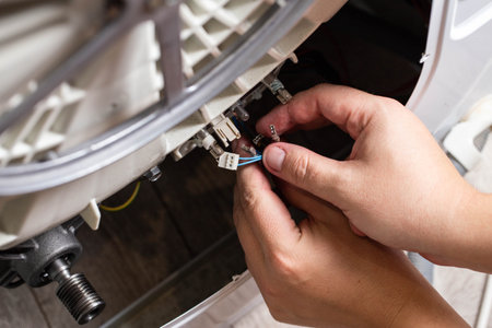 The hand of the master removes the electrical chips to remove the heating element of the washing machine and the heating sensor. Repair of washing machines, close-upの写真素材