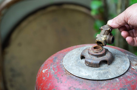 A broken valve of a gas cylinder in a hand against the background of a red gas cylinder. Propane gas leak and explosion concept.の写真素材