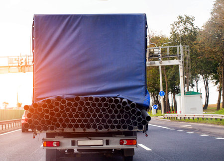 A tilt van transports an oversized cargo of metal pipes along the road against the backdrop of a sunset.の写真素材