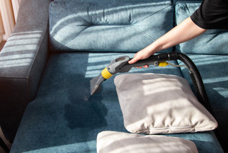 A girl's hand with a professional washing vacuum cleaner cleans white pillows from dirt on the sofa. Cleaning services, industryの写真素材