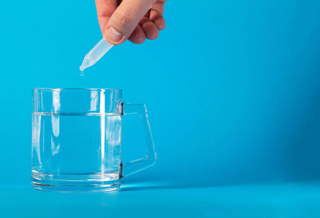A drop of medicine from a tube drips into a mug of water on a blue background. Concept of treatment with metabiotics, prebiotics and probiotics. Restoration of intestinal microflora during dysbacteriosis.の写真素材