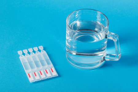 a cup of water and tubes with a new generation metabiotic on a blue background. Treatment of the intestines, restoration of microflora after dysbacteriosis.の写真素材