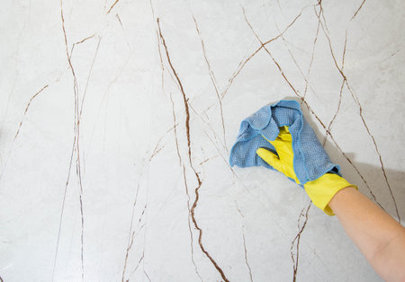 Washing porcelain tiles on the wall in the bathroom, a hand in a yellow glove with a rag, close-up. Copy space for textの写真素材