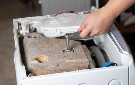 A washing machine repairman tightens the counterweight in the washing machine due to noise and vibration. Copy space for text, disassemblingの写真素材