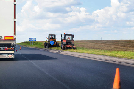 a grader repairs the side of the road and a tractor mows the grass on the side of the road, organizations engaged in road repair and maintenanceの写真素材