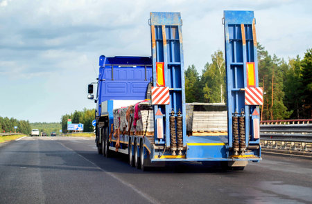 A modern blue tractor with a semi-trailer trawl transports cargo along the highway in the summer. Copy space for text.の写真素材