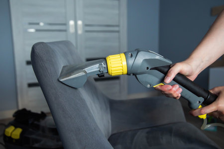A girl s hand with a washing vacuum cleaner cleans the gray upholstery of a fabric chair in the apartment from dirt. Cleaning services, upholstered furniture cleaningの写真素材