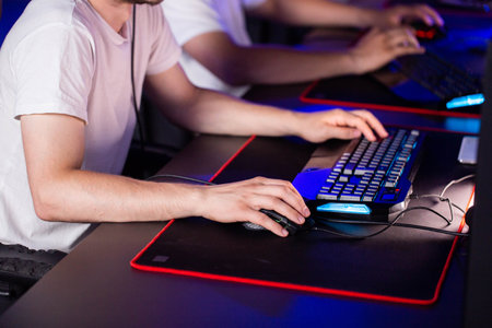 Gamer plays video game on PC at computer club with his team, professional cyber sport tournament, gaming mouse RGB lighting keyboard on mat close up. E-sport championship.の写真素材