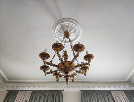 Copper chandelier with light bulbs in the form of candles on a white ceiling in a museum, close-upの写真素材