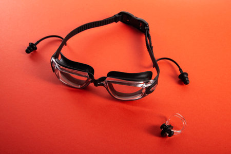 Swimming goggles and pool cap with nose clip on red background, isolateの写真素材