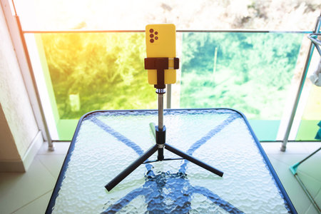 A yellow phone smartphone stands in a phone stand on the table. The concept of communicating from a phone via video calling and the Internetの写真素材