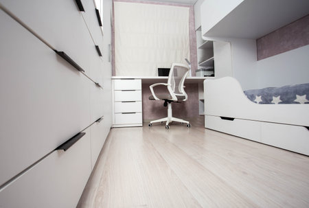 Interior of a modern children's bedroom with a bunk bed, a chest of drawers and a table with a laptop and a computer chair. White bedroom interior, blinds.の写真素材