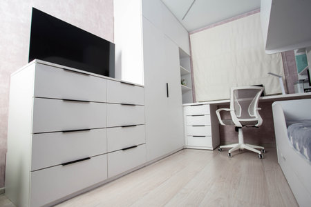 Modern workplace in the bedroom with white furniture, computer desk and chair. The TV is on a white chest of drawers. Bedroom beautiful interior.の写真素材