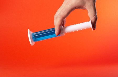 Hand holding a blue syringe on a red background. Copy space for textの写真素材