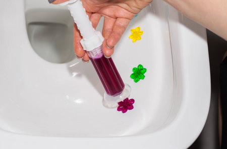 Burgundy gel in a syringe in a hand in the toilet bowl of a toilet in the form of flowers. Antibacterial and disinfectant effect, close-up. Copy space for text, eco-friendly productの写真素材