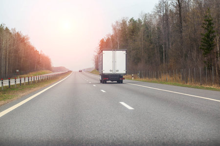 a manufactured goods van transports non-food cargo along a highway in the spring against the backdrop of the sun. Copy space for textの写真素材
