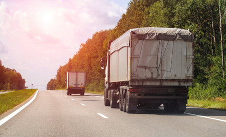 A truck with a semi-trailer for bulk agricultural cargo transports grain along a highway in summer,...