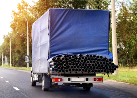 Transportation of metal pipes in a truck on a road in summer against the backdrop of the sun,...