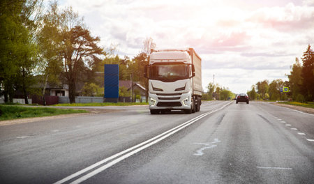 A modern white truck transports expensive cargo in a covered semi-trailer against the backdrop of a...