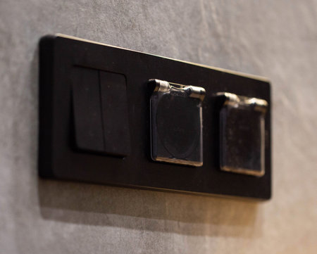 triple closed black socket with switch on gray tiled wall background