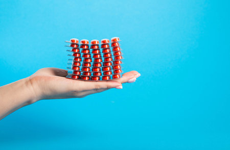 Stack of red pills on palm in hand on blue background. Concept of fluoroquinolone antibiotic pills in treatment of diseases. Copy space for textの写真素材