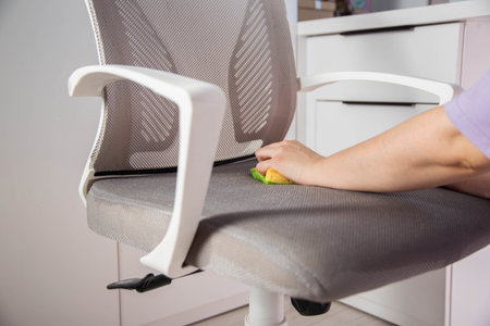 Womens hands wash dirty spots from gray upholstery of computer chair. Concept of dry cleaning of...