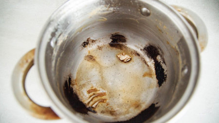 Burnt food in a saucepan, close-up. Black burnt food deposits on non-stick coating.