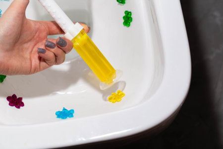 Yellow gel in a syringe in a hand against the background of a toilet. Toilet cleaning and...