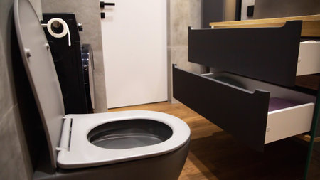 Gray wall hung toilet against white door and wall hung cabinet with pull out shelves in bathroom.
