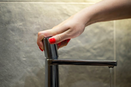 Female hand with red manicure turns on water in modern chrome faucet with floating head