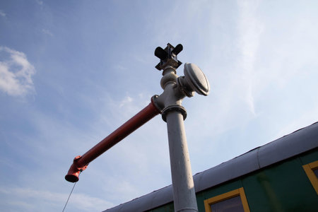 A bright day showcases a railroad signal standing tall near a vintage train. The signal, colored...
