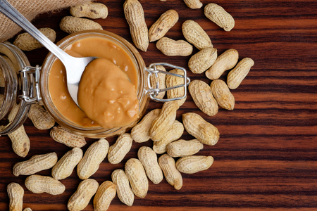 Organic peanut butter paste on metal spoon and scattered nuts on tableの写真素材