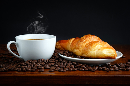 French breakfast: croissant bread and black coffee with coffee beans on tableの写真素材