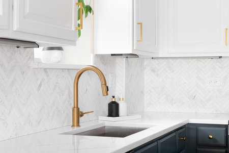 Sink detail shot in a luxury kitchen with herringbone backsplash tiles. white marble countertop, and gold faucet.の写真素材