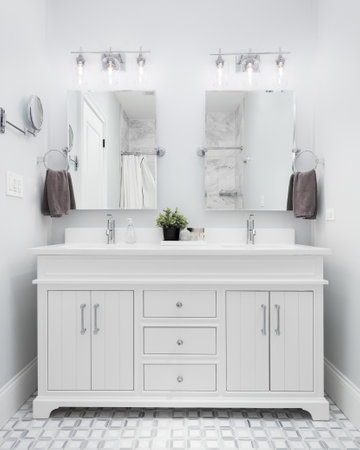 An elegant bathroom with a white vanity cabinet, chrome lights mounted above the double mirrors, and a beautiful mosaic tile floor.の写真素材