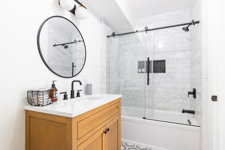 A beautiful bathroom with a wood vanity, custom tile shower and floor, and a sliding glass door with...