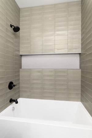 A shower with brown subway tile walls, small hexagon tiles in the shelf, and black shower head and...