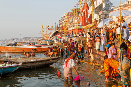 Showing the colorful traditional clothing and Hindu religious ritual of bathing in the holy Ganges River from the ancient ghats of Varanasi.のeditorial素材