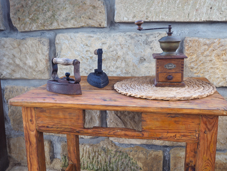 two old rusty antique iron with wooden handle, hand coffee grinder on old wooden side table with sandsotone wall backgroundの写真素材