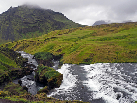 river cascade  in green grass and mossed stones on the iceland trek with fogの写真素材