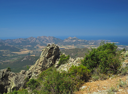 sharp stones mountain sea view with a blue sky and green bushesの写真素材