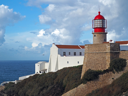 red lighthouse on Cabo de Sao Vicente with stone wall  and white houseの写真素材