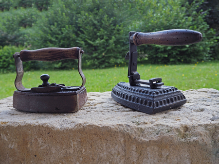 two old rusty antique iron with wooden handle on sandstone wall with organic green backgroundの写真素材